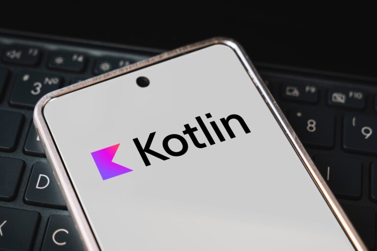 Telefon komórkowy z logo Kotlin na ekranie, leżący na klawiaturze laptopa.