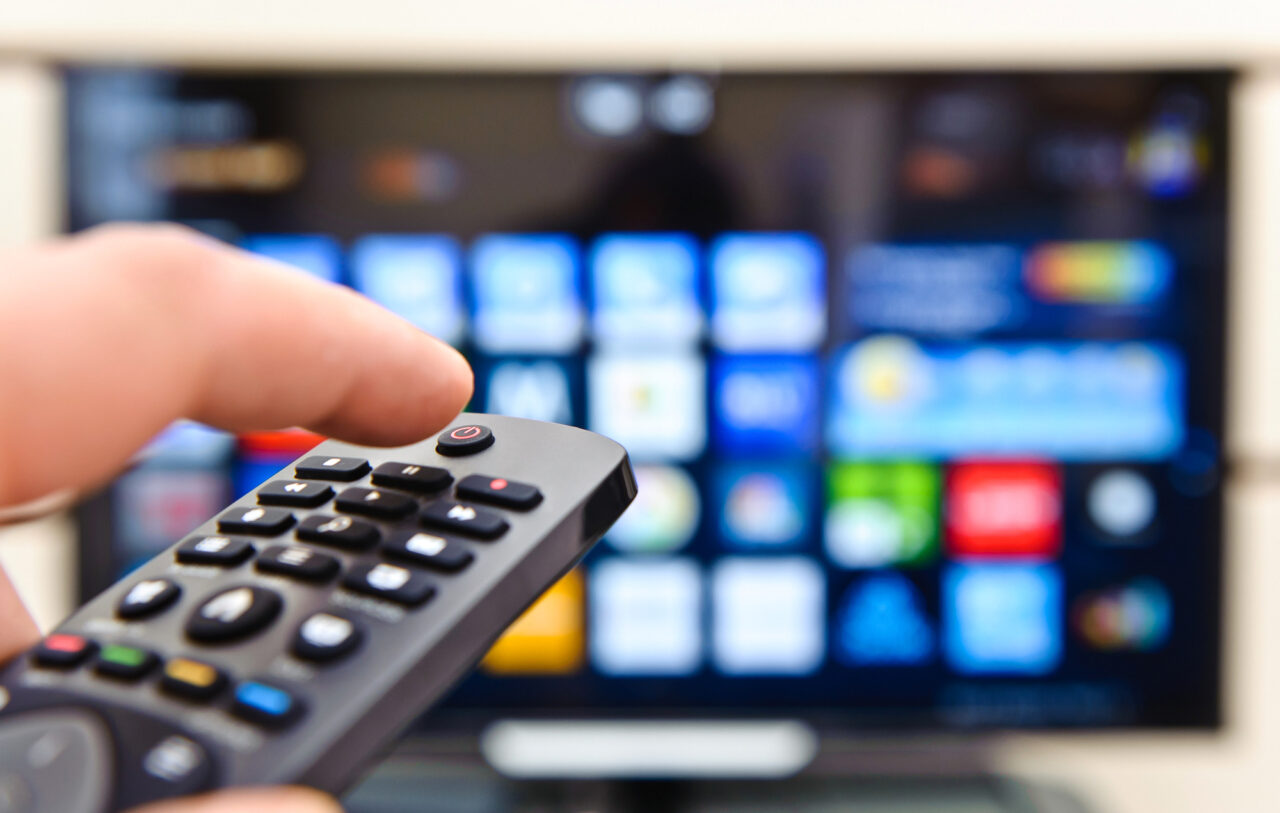Telewizja cyfrowa w nowym wydaniu. Brazylia wprowadza w życie standard TV 3.0. Pierwszy plan zdalnego sterowania telewizorem kierowanego w stronę ekranu telewizora wyświetlającego kolorowe ikony aplikacji.