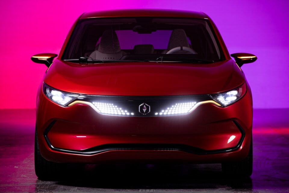 Czerwony samochód elektryczny z logo w kształcie rombu na środku kratki, oświetlony na fioletowo-różowym tle.