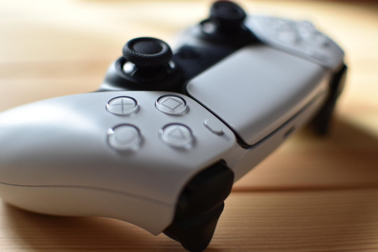 Biało-czarny bezprzewodowy kontroler do gier DualSense z przyciskami i analogami, położony na drewnianym blacie.