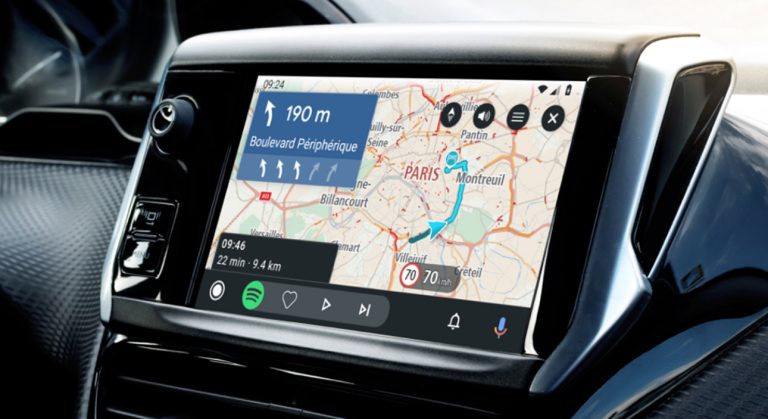 Wyświetlacz nawigacji samochodowej pokazujący mapę Paryża z aktywną trasą i zbliżającym się manewrem, a także ikony aplikacji Spotify i ustawień.