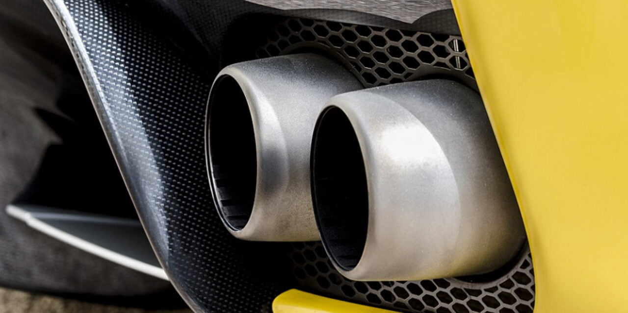 Podwójne końcówki wydechu z metalu umieszczone w żółtym tyle samochodu sportowego z elementami z włókna węglowego. Strefa Czystego Transportu w Warszawie