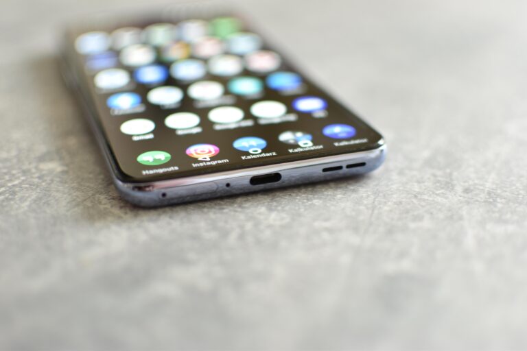 Smartfon leżący na szarym podłożu z widocznym ekranem pokazującym kolorowe ikony aplikacji.