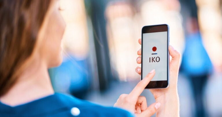 Kobieta używa aplikacji IKO na swoim smartfonie na zatłoczonym miejskim tle.