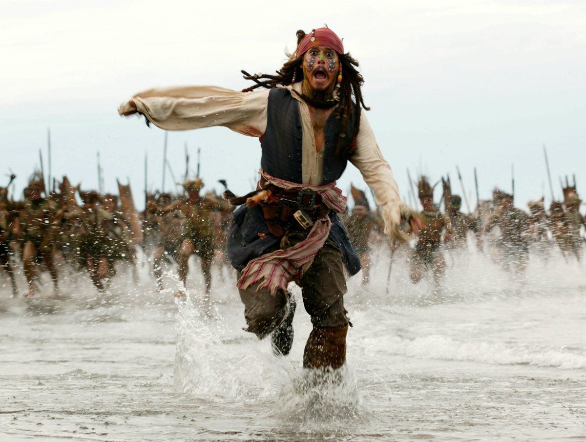 Johnny Depp w pirackim stroju ucieka przez płytką wodę, wyraźnie przerażona, z tłumem uzbrojonych ludzi w odległości, goniących ją.
