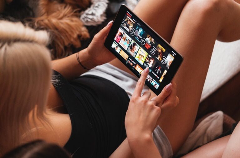 kobieta trzymająca na kolanach tablet z uruchomioną aplikacją Netflix