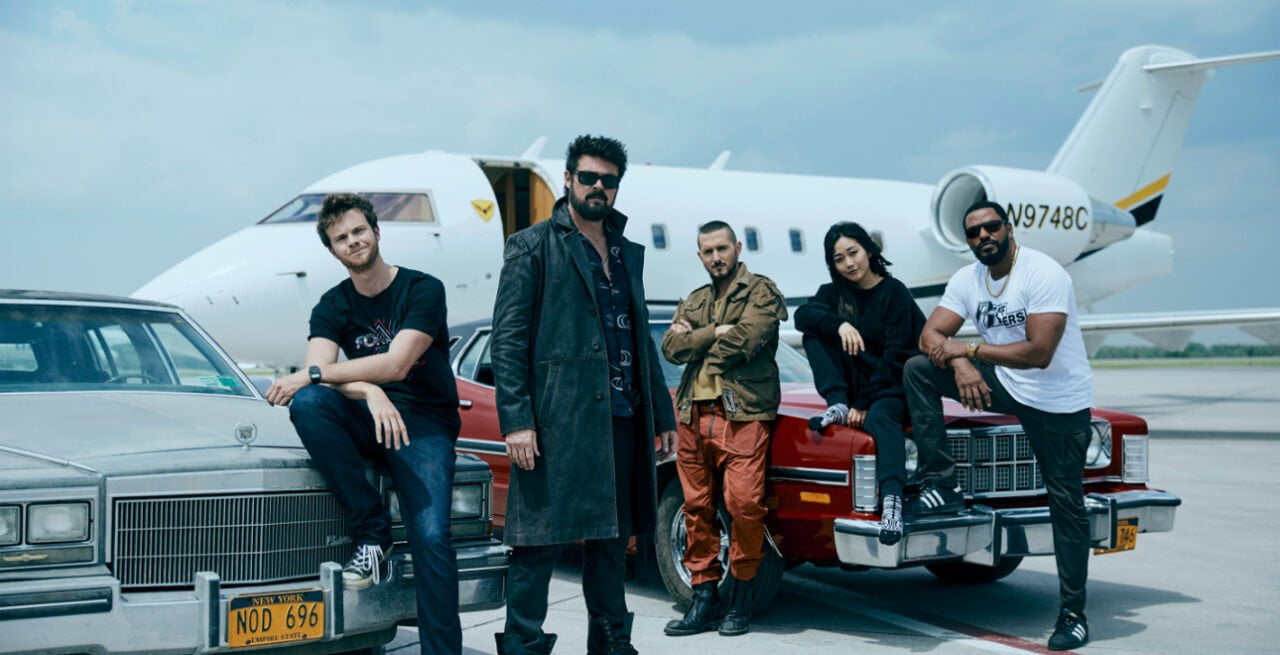 Czwarty sezon The Boys. Kadr z serialu The Boys. Pięcioosobowa grupa stoi obok czerwonego samochodu klasycznego i białego prywatnego odrzutowca na płycie lotniska.