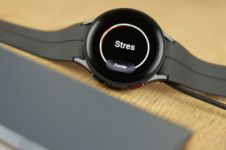 Czarny inteligentny zegarek na drewnianej powierzchni z ekranem pokazującym aplikację do monitorowania stresu z napisem "Stres" i przyciskiem "Pomiar" na wyświetlaczu.