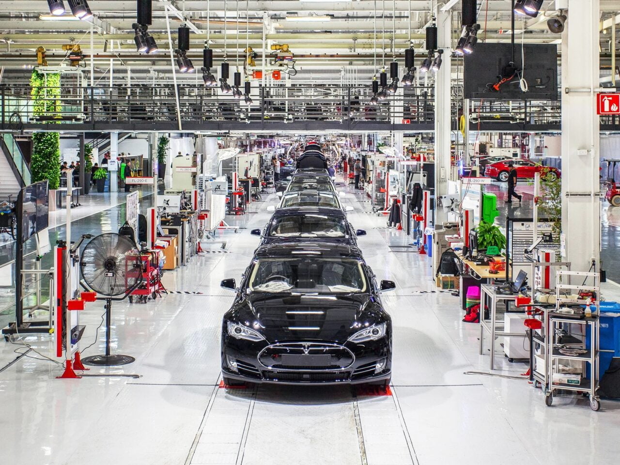 Samochody elektryczne wprowadziły przemysł motoryzacyjny w kryzys? Linia montażowa w fabryce samochodów z czarnymi autami i rozmieszczonymi stanowiskami pracy.