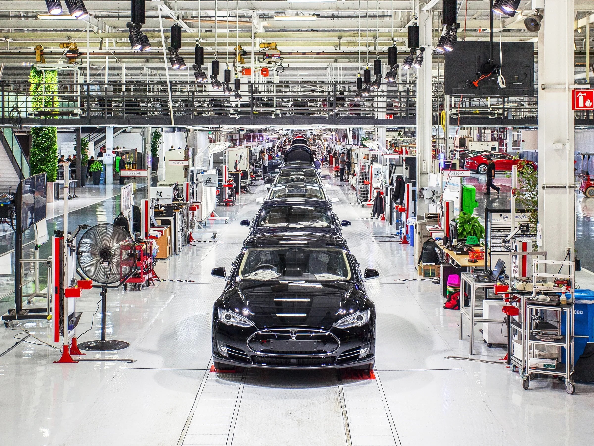 Linia montażowa w fabryce samochodów z czarnymi autami i rozmieszczonymi stanowiskami pracy.