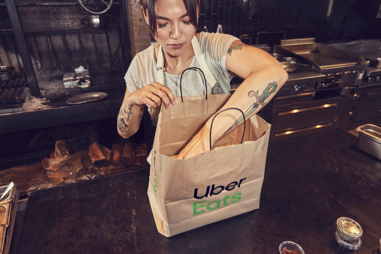 Kobieta pakuje jedzenie do siatki Uber Eats, przez co Uber zarabia. 