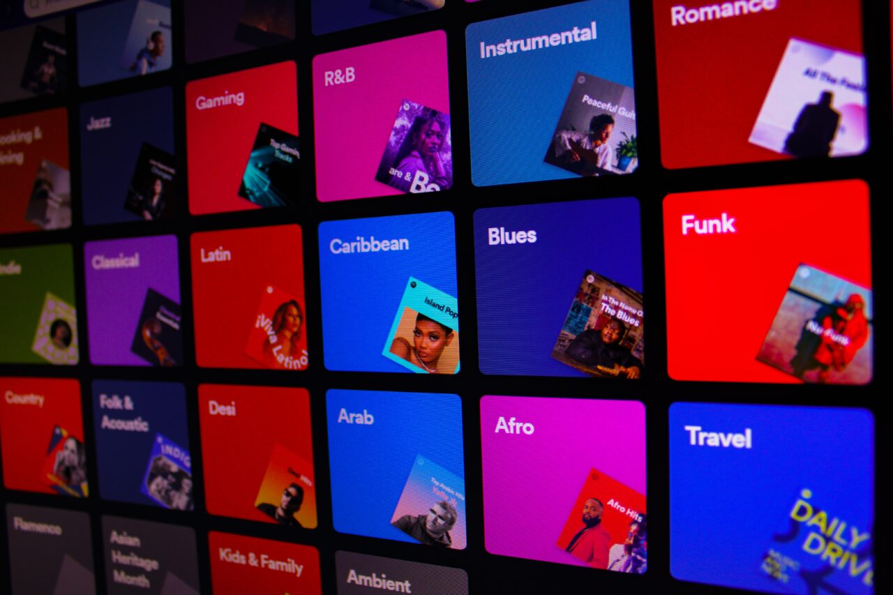Różnokolorowe kwadraty z nazwami różnych gatunków muzycznych i odpowiadającymi im grafikami artystów na ekranie cyfrowym.