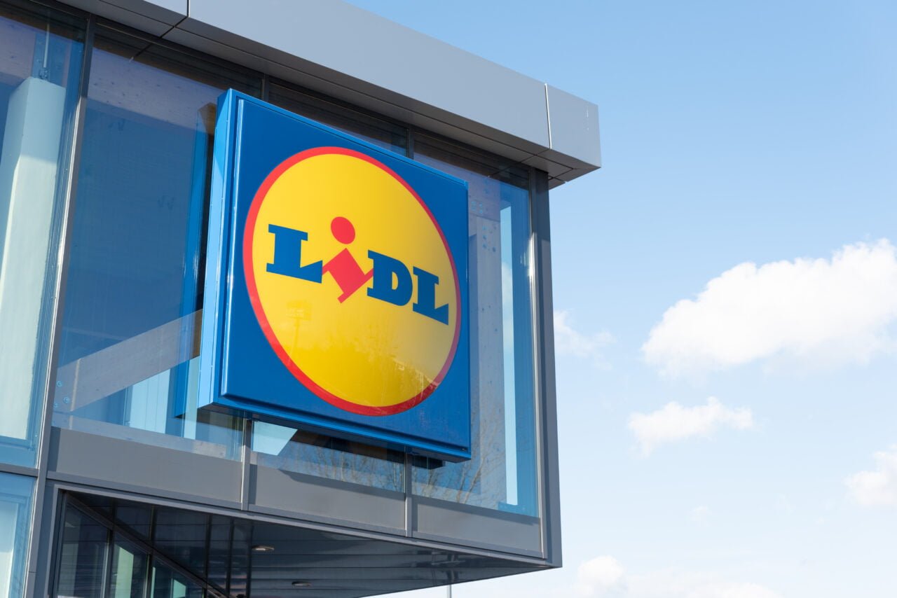 O logotipo da rede de lojas Lidl na fachada do prédio contra um céu azul com pequenas nuvens.