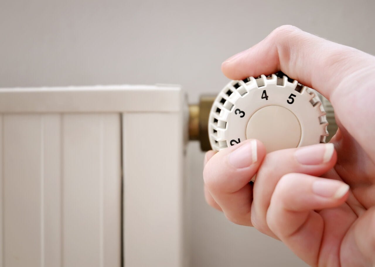 Osoba reguluje termostat grzejnika, ustawiając pokrętło na wyższą temperaturę.
