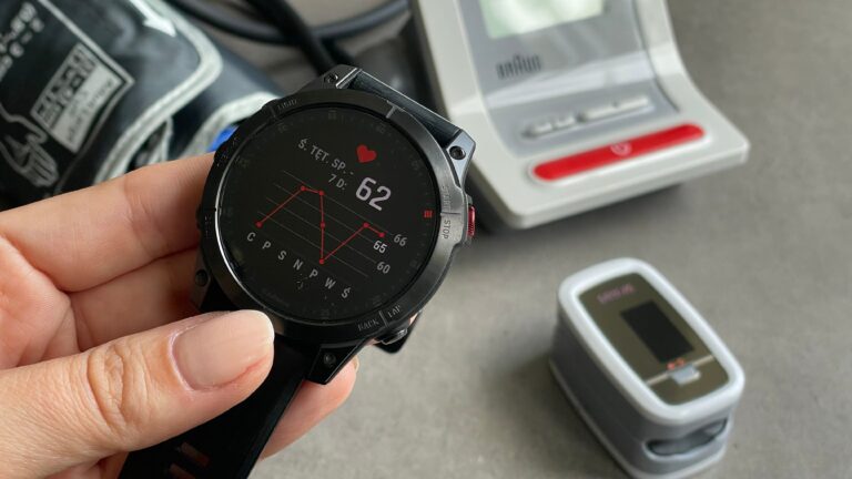 Zegarek sportowy na nadgarstku z wyświetlonym pulsometrem i krokomierzem, w tle rozmyte urządzenia do monitorowania aktywności fizycznej.
