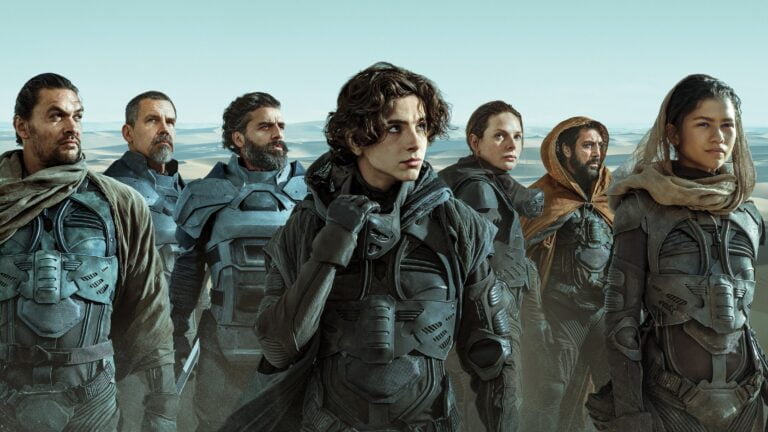 Grupa ludzi w futurystycznych strojach bojowych na tle pustynnego krajobrazu.