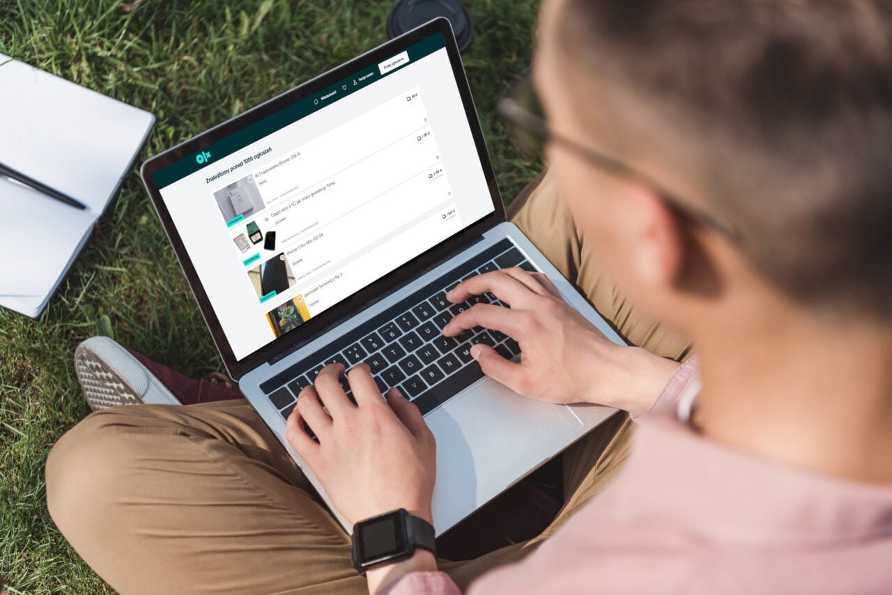 Mężczyzna pracujący na laptopie siedząc na trawie, z widokiem na ekran pokazujący interfejs użytkownika strony internetowej.