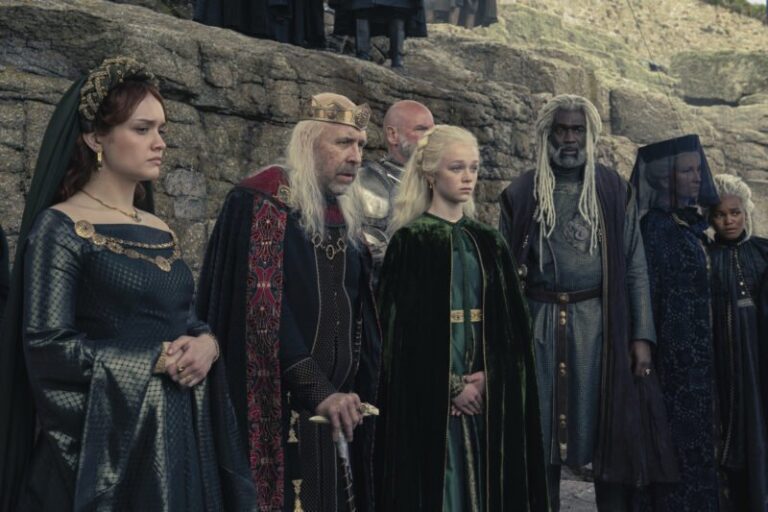 Kadr z serialu Ród smoka. Grupa osób w średniowiecznych strojach stoi na skalnym wybrzeżu, wśród nich król w koronie, młoda kobieta w zielonej sukni i inne postacie w szatach szlacheckich.