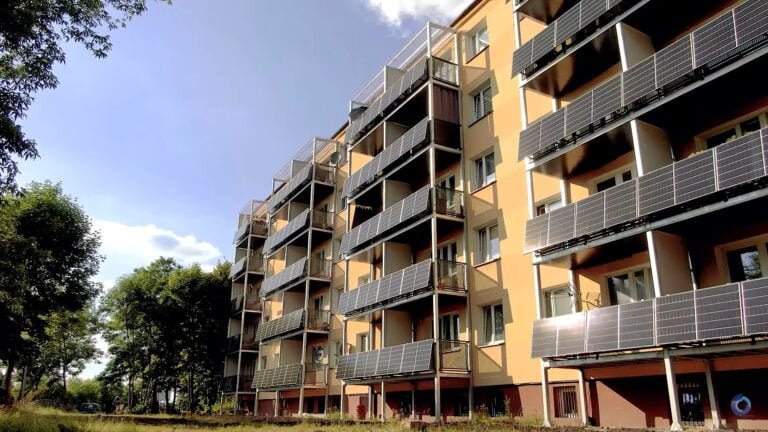 Wielopiętrowy budynek mieszkalny z balkonami i panelami słonecznymi umieszczonymi na zewnątrz.