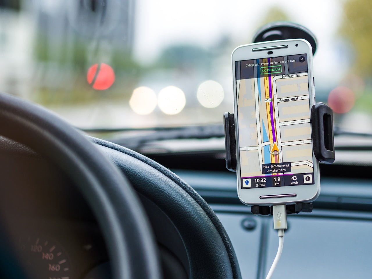 biały smartfon z włączoną nawigacją samochodową zamocowany w uchwycie samochodowym, który jest przyczepiony do szyby auta