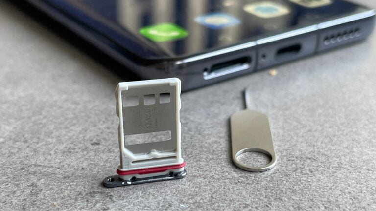 smartfon leżący na blacie z wyciągniętą tacką na kartę SIM, obok kluczyk do tacki
