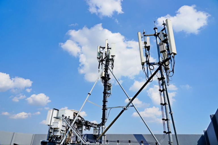 Anteny komórkowe operatora umieszczone na metalowej konstrukcji na tle niebieskiego nieba z chmurami.