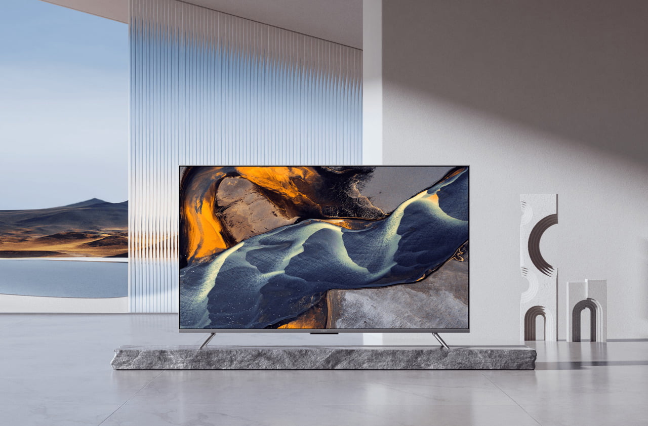 telewizor Xiaomi QLED TV Q2 stojący z nowoczesnym wnętrzu w kolorach szarości. W tle widać krajobraz gór i czyste niebo