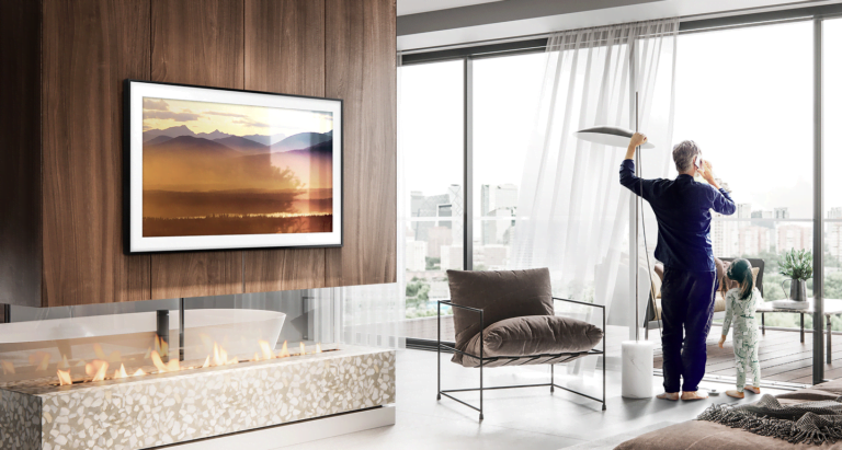 telewizor Samsung The Frame wiszący na ścianie w salonie. Po prawej stronie widać mężczyznę rozmawiającego przez telefon i patrzącego za okno