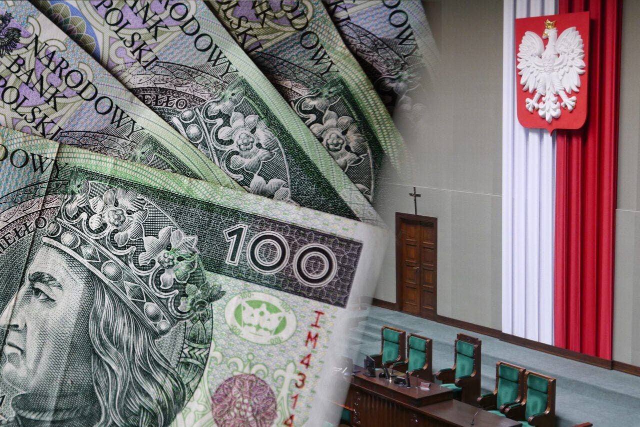 Zdjęcie przedstawiające banknoty o nominale 100 zł z wizerunkiem króla Władysława Jagiełły na pierwszym planie z rozmytym tłem, na którym widać fragment polskiego sejmu, w tym mównicę i polskie barwy narodowe biało-czerwone za pulpitem prezydialnym.