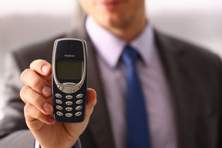 Mężczyzna w garniturze i niebieskim krawacie trzymający w dłoni klasyczny telefon komórkowy Nokia.