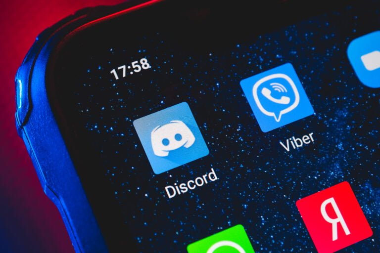 Zbliżenie na ekran smartfona z widoczną ikoną aplikacji Discord, otoczonymi przez inne ikony aplikacji, na czerwono-niebieskim tle.