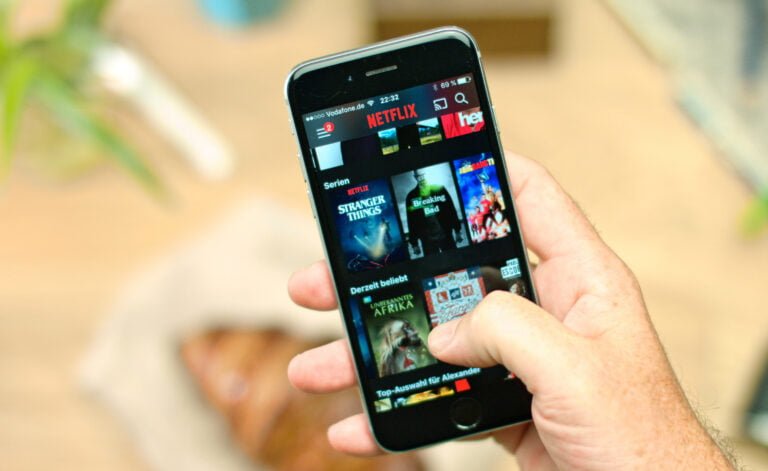 Osoba trzymająca smartfon z uruchomioną aplikacją Netflix wyświetlającą popularne seriale i filmy.