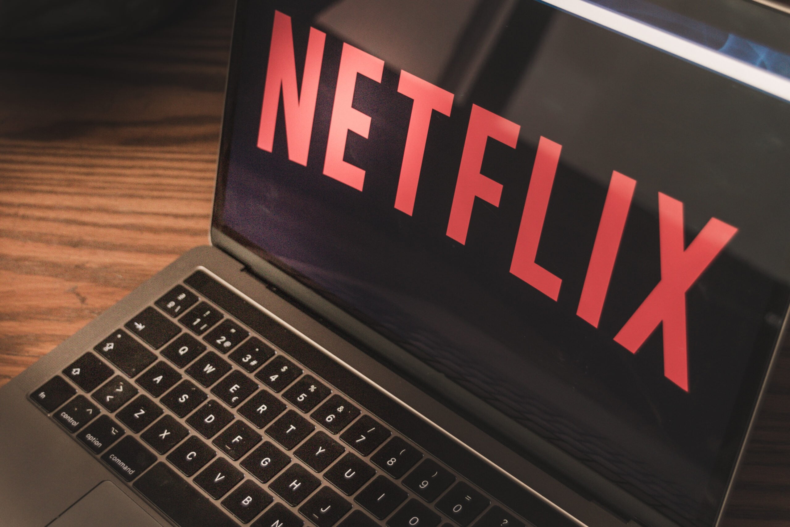 Laptop na drewnianym biurku z ekranem wyświetlającym logo Netflix w czerwonym kolorze na czarnym tle.
