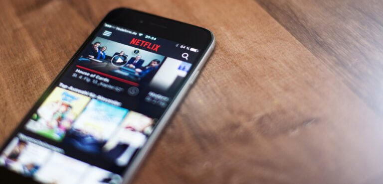 Smartfon leżący na drewnianym blacie z otwartą aplikacją Netflix na ekranie.