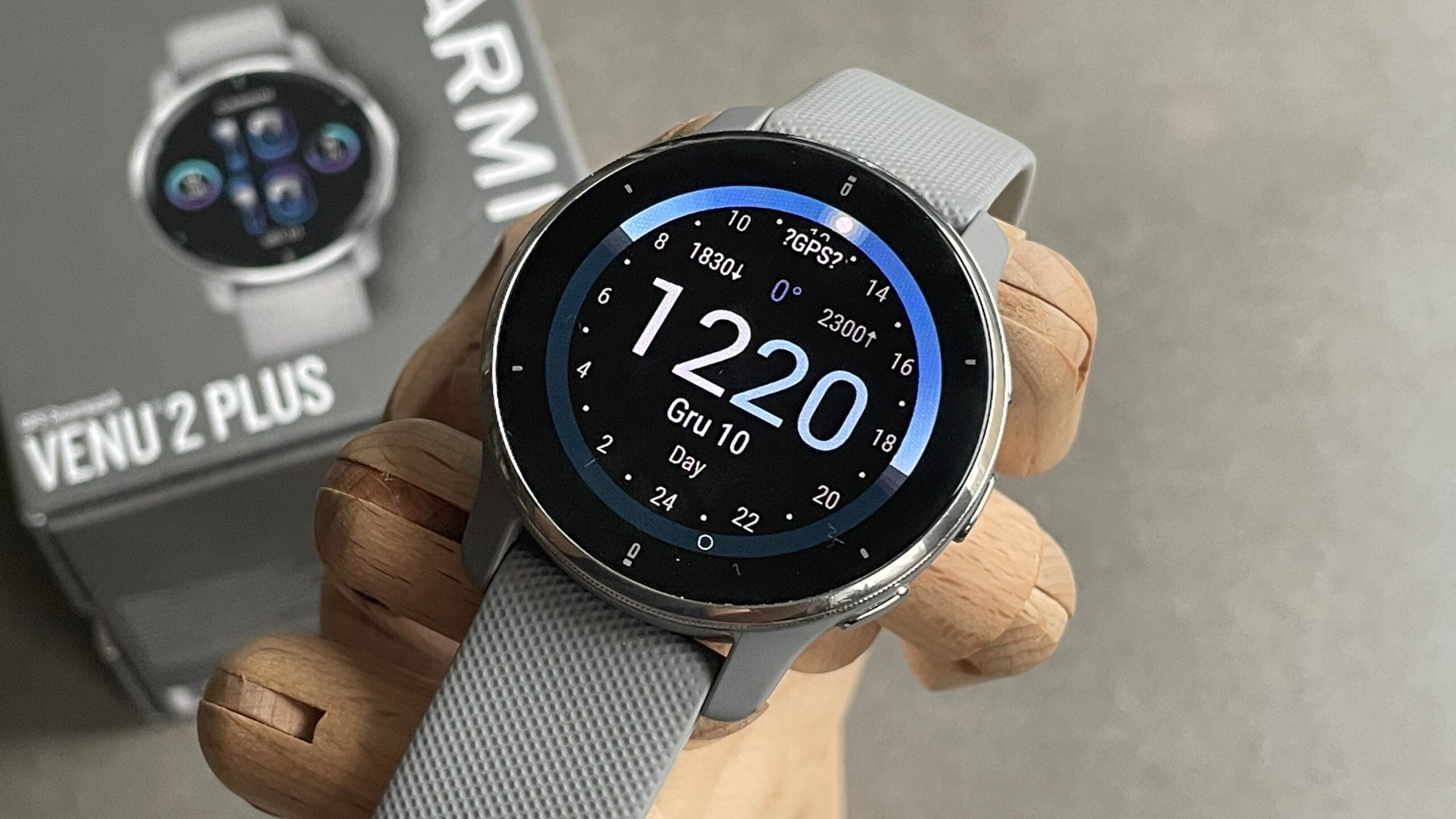 Inteligentny zegarek Garmin Venu 2 Plus na drewnianym stojaku, z cyfrową tarczą pokazującą godzinę 12:20 i datę "Gru 10".