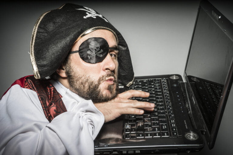 Mężczyzna przebrany za pirata z czarną opaską na oku siedzi przed laptopem.
