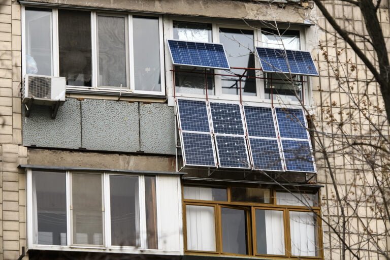 Panele słoneczne zamontowane na balkonie starego bloku mieszkalnego obok klimatyzatora.
