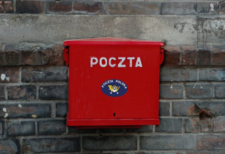 Czerwona skrzynka pocztowa z napisem "POCZTA" i logotypem Poczta Polska na kamiennym murze.