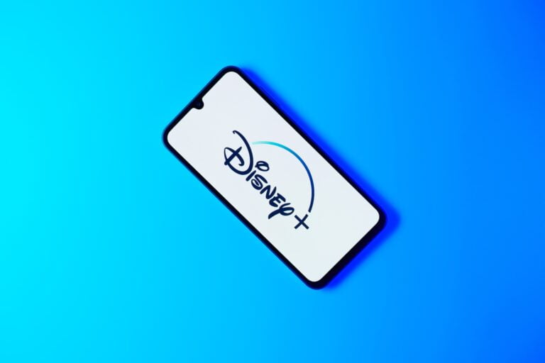 Smartfon z logo Disney+ na ekranie, leżący na niebieskim tle.