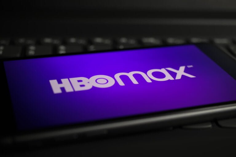 smartfon leżący na klawiaturze komputera. Na ekranie smartfona widać logo HBO Max na fioletowym tle