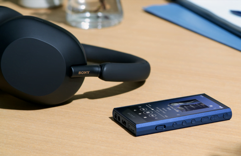 Czarne słuchawki Sony na biurku obok niebieskiego przenośnego odtwarzacza muzyki Sony.