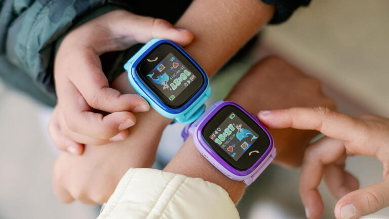 Dwa dziecięce smartwatche na nadgarstkach, jeden niebieski i jeden fioletowy, oba wyświetlające animacje i kroki.
