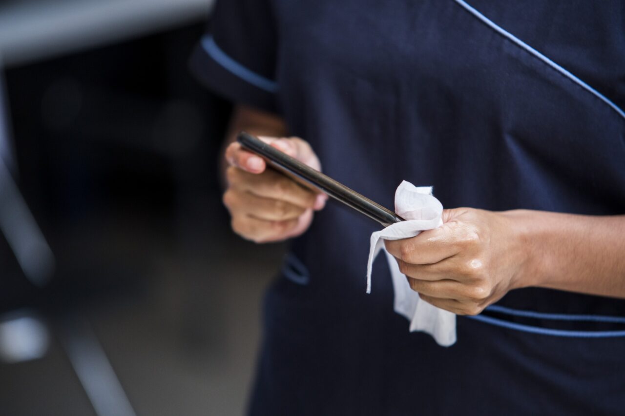 Jak wyczyścić telefon? Osoba w granatowym ubraniu czyści smartfon białą ściereczką.