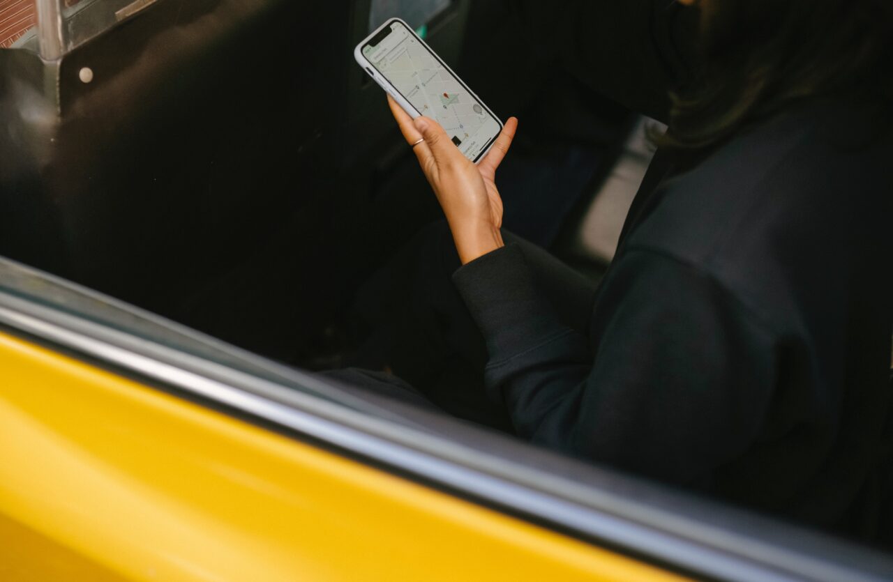 Osoba w czarnym ubraniu trzymająca smartfona z otwartą aplikacją mapy w środku transportu z żółtymi elementami.
