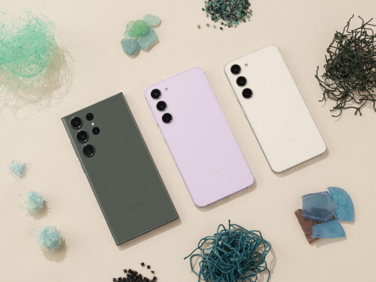 Trzy smartfony Samsung z tyłu, każdy z zestawem aparatów, leżące na neutralnym tle z otaczającymi je dekoracyjnymi elementami, takimi jak kawałki szkła i kolorowe nici.
