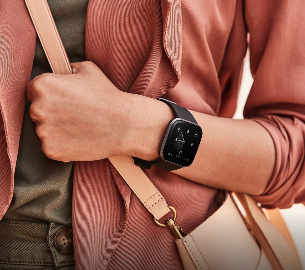 Opis obrazu: Osoba w czerwonawym płaszczu nosi czarny smartwatch na nadgarstku.