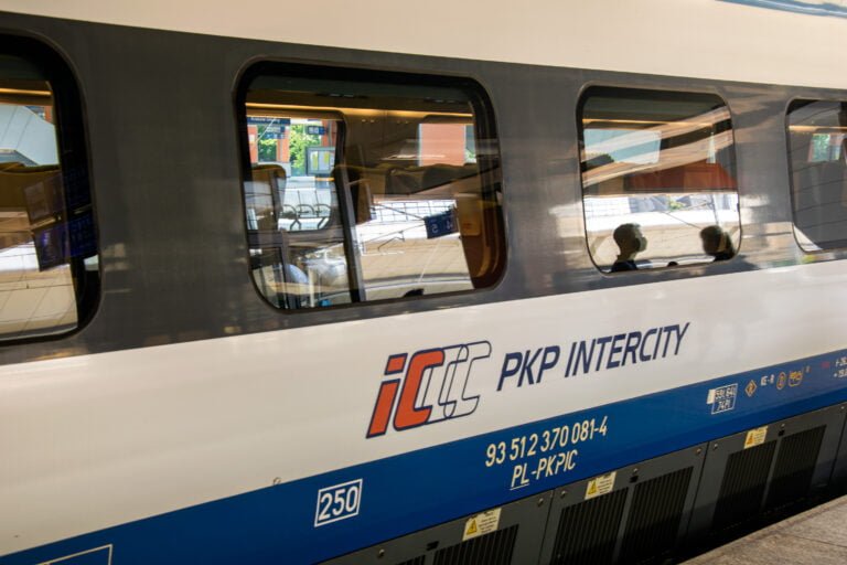 Pociąg PKP Intercity na peronie, widoczne logo oraz fragment wnętrza przez okno.