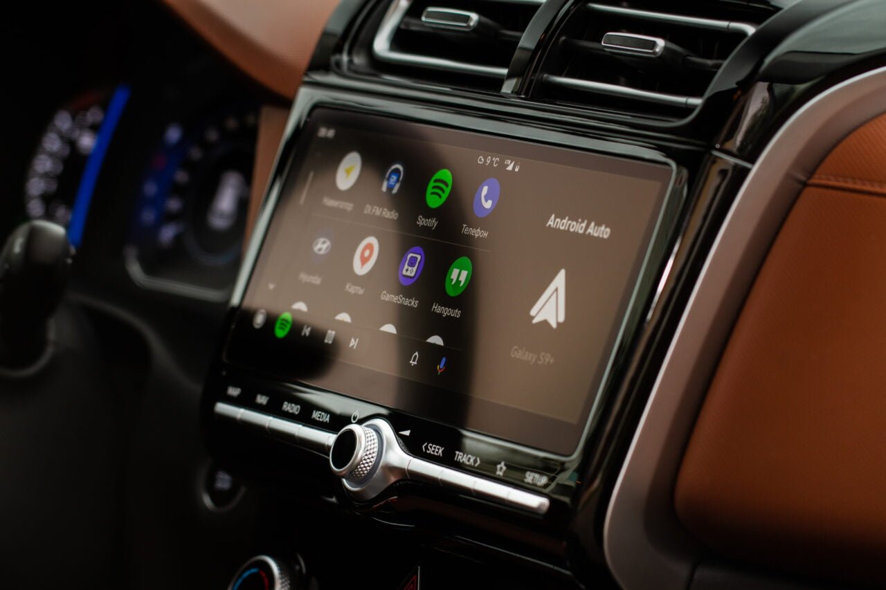Ekran systemu multimedialnego Android Auto wyświetlający aplikacje w samochodzie z brązową tapicerką.