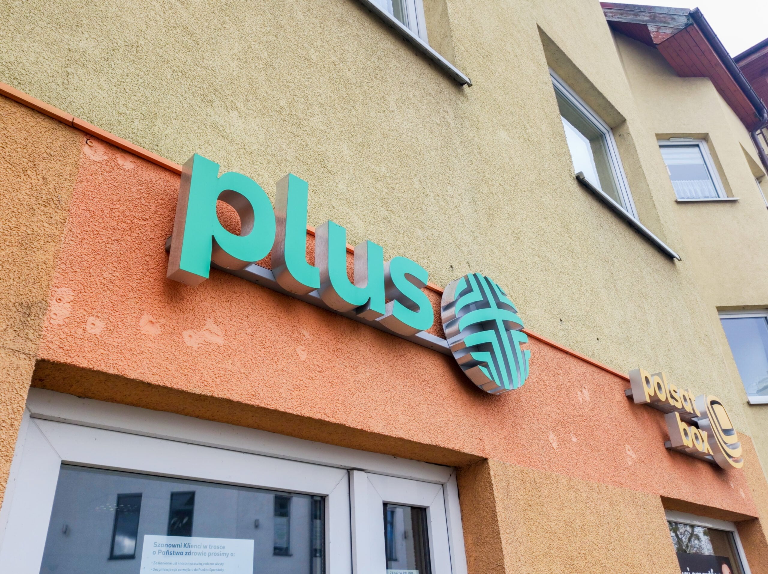 Napis na elewacji budynku z logo "Plus" i napisem "Poczta Polska" w słoneczny dzień.