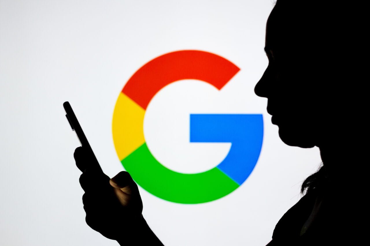 Sylwetka kobiety trzymającej smartfon na tle wyświetlanego logo Google AI Cyber Defense